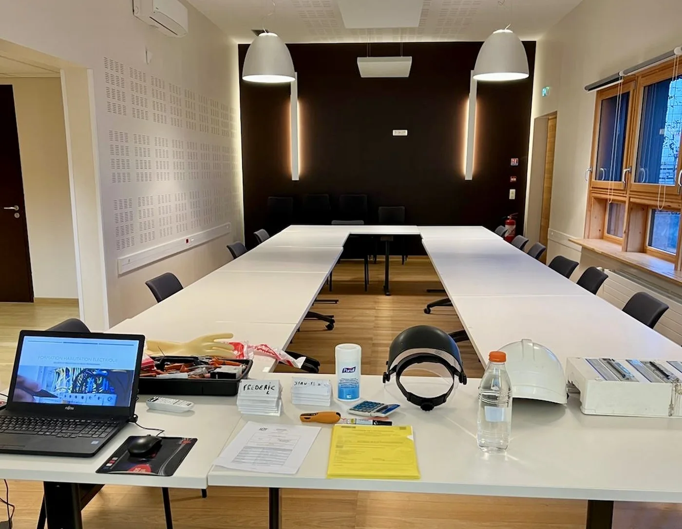 Salle de formation réservée par NB Formation pour une session habilitation électrique : tables en U, et sur la table du formateur le support de cours, les gants isolants, l'écran facial, le casque, la caisse d'outils isolés et le tableau électrique pédagogique